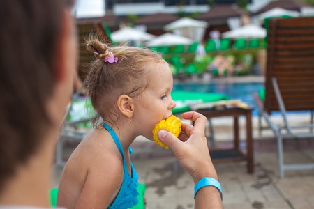 Young father feeds his little daughter corn near the swimming poolの写真素材