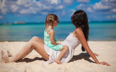 Young beautiful mother and her little daughter on white beachの写真素材