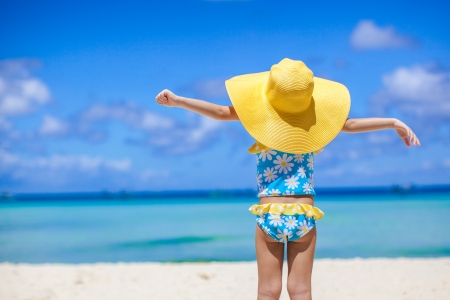 Rear view of baby girl in big hat looking at the sea on white sand beachの写真素材