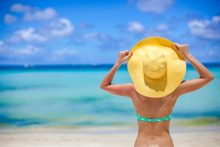 Young slim woman sitting on beach holding yellow hatの写真素材