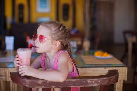 Adorable little girl having breakfast and drinking fruit cocktailの写真素材