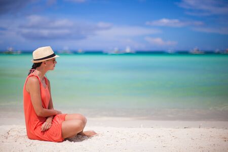 Rear view of young sexy woman in hat sitting on white sand beachの写真素材