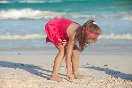 little cute girl draws on the white sand at tropical beachの写真素材