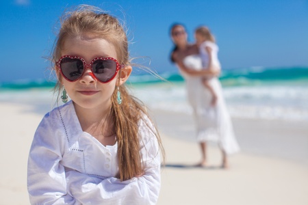 Portrait of cute adorable girl and her mother with little sister in the background at tropical beachの写真素材