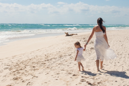 Back view of young mother and her cute daughter walking on exotic beachの写真素材