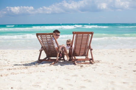 Young father and his wonderful daughter sitting on beach wooden chairs looking at cameraの写真素材
