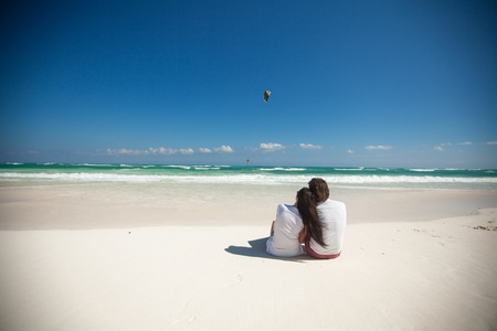 Back view of young couple sitting at tropical white beachの写真素材