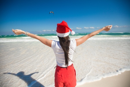 Back view of beautiful girl in santa hat walking like a bird on white beachの写真素材