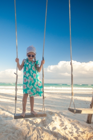 Little cute girl in dress riding a seesaw on the beachの写真素材