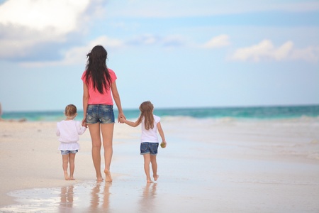 Back view of young mother and her cute daughters walking at tropical beachの写真素材