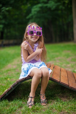 Cute little girl in purple Happy Birthday glasses smiling in parkの写真素材