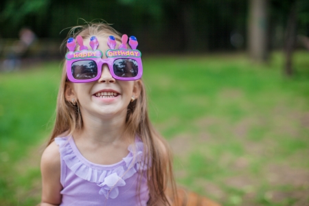 Adorable little girl in Happy Birthday glasses smiling outdoorの写真素材