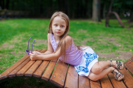 Cute little girl lying on wooden chair and relaxing outdoor in the parkの写真素材