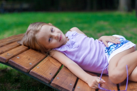 Cute little girl lying on wooden chair outdoor in the parkの写真素材