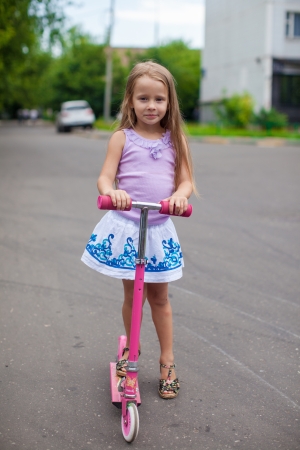 Fashion adorable little girl on a scooter on the streetの写真素材