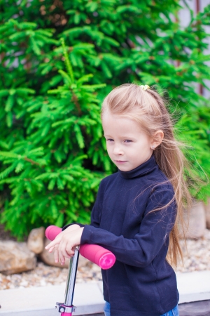 Adorable little girl on a scooter in the yardの写真素材