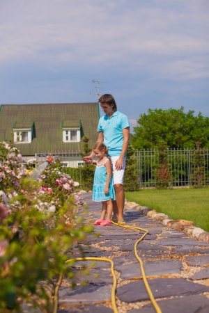 Little cute girl and father watering flowers with hose in their gardenの写真素材