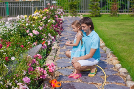 Adorable girl and young father watering flowers with hose in their gardenの写真素材