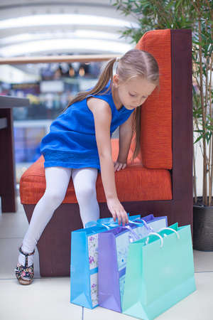 Little fashion girl sits near packages in a large shopping centerの写真素材