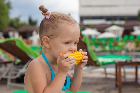 Cute little girl eating corn at the pool on vacationの写真素材