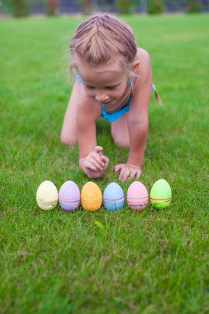Beautiful little girl counts Easter eggs on green grassの写真素材