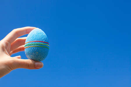 Bright blue Beautiful Easter egg in hand on background of blue skyの写真素材