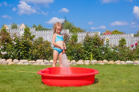 happy little girl pouring water from a hose and laughingの写真素材