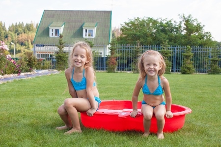 Two little sisters frolicing and splashing in their yard in small poolの写真素材