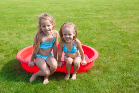 Two little sisters frolicing and splashing in their yard in small poolの写真素材