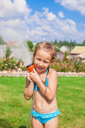 happy little girl pouring water from a hose and laughingの写真素材
