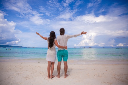Back view of young couple spread their arms standing on white sandy beachの写真素材