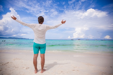 Back view of young man spread his arms standing on white sandy beachの写真素材
