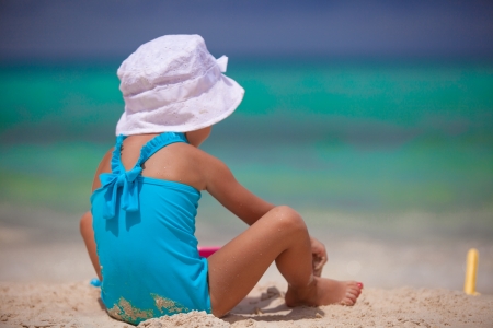 Back view of little girl in nice swimsuit playing on sandy beachの写真素材