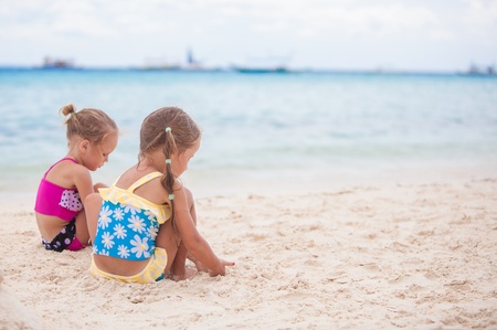 Two little sisters in nice swimsuits playing on sandy beachの写真素材
