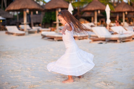 Adorable little girl in beautiful clothes dancing at sunset beachの写真素材