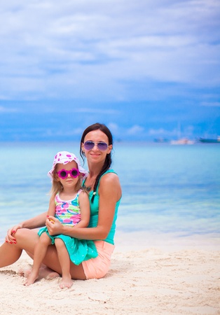 Young beautiful mother and her little daughter sitting on white beachの写真素材
