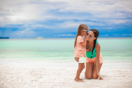 Young mother and her cute little girl whispering on the white beachの写真素材