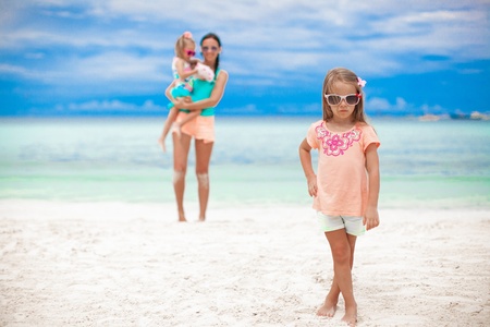 Portrait of adorable girl and her mother with little sister in the background at tropical beachの写真素材