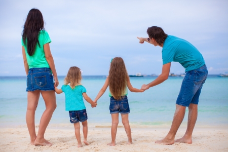 Back view of young family with two daughters at exotic beach on sunny dayの写真素材