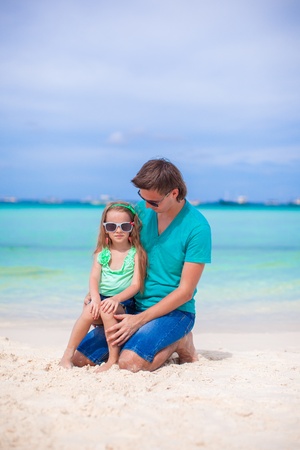 Young father and his little daughter sitting on tropical white sand beachの写真素材