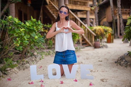 Young girl sitting on sand with the word "Love" and making heart by her handの写真素材