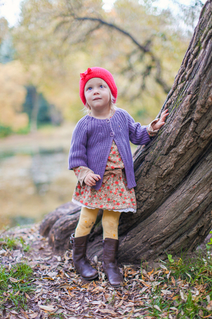Cute little girl in a red cap near lake in the autumn parkの写真素材
