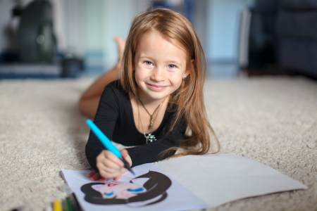 Portrait of a sweet charming young girl who draws with his coloring at homeの写真素材
