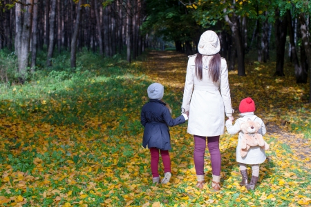 Back view of young mother and her cute little daughters walking on autumn meadow at sunny dayの写真素材
