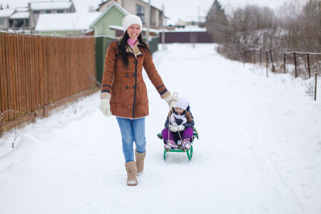Young mother rolls her little cute daughters on a sled in winter dayの写真素材
