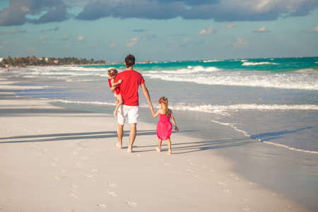 Back view of young father and his cute daughters walking along the seaの写真素材