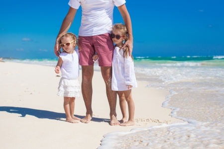 Young happy father and little daughters having fun on white beach in sunny dayの写真素材
