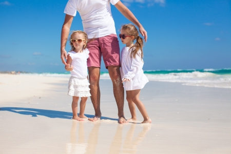 Young happy father and little daughters having fun on white beach in sunny dayの写真素材