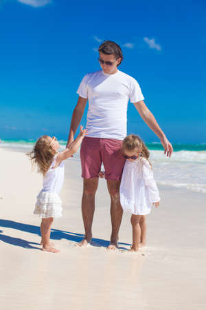 Young happy father and little daughters having fun on white beach in sunny dayの写真素材