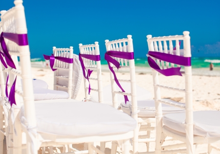 White wedding chairs decorated with purple bows on sandy beachの写真素材